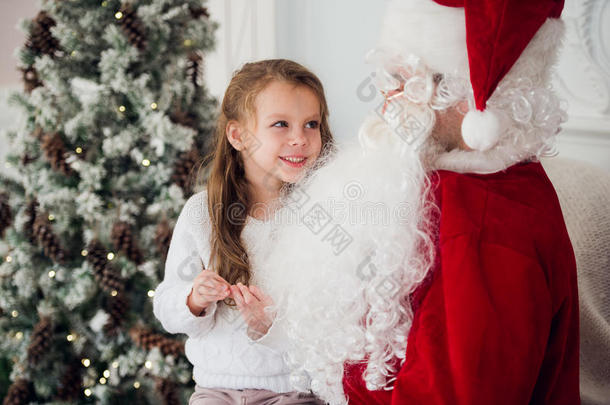 梦想在圣诞节是真实的。 快乐的小可爱女孩坐在<strong>年迈</strong>的圣诞老人的膝上，在家里附近拥抱