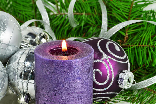 带有蜡烛和装饰品的圣诞节背景。 紫色和银色的圣诞球在雪中的冷杉树枝上