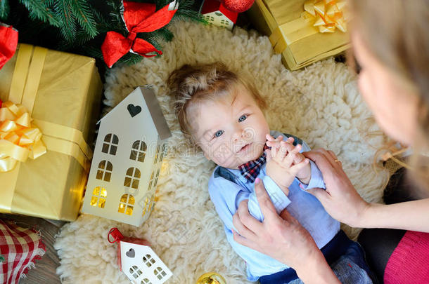 可爱的小婴儿肖像庆祝圣诞节。 新年`假期。 男孩躺在树下和妈妈玩