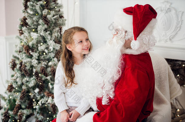 梦想在圣诞节是真实的。 快乐的小可<strong>爱女</strong>孩坐在年迈的圣诞老人的膝上，在家里附近拥抱