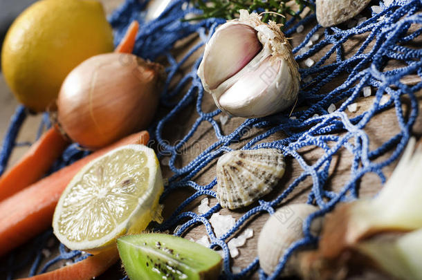 烹饪背景。 木制背景上的大蒜，洋葱，胡萝卜，柠檬。 海上风格，蓝色渔网和贝壳。