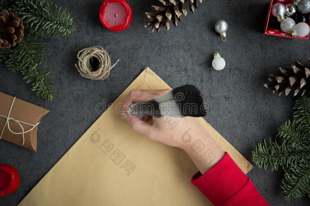 女孩在灰色背景上用墨水笔在黄色纸上用圣诞装饰品给圣诞老人写信。