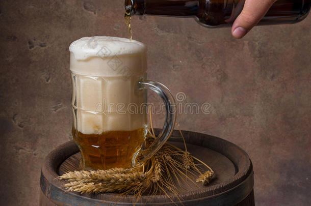 啤酒杯，麦穗在木桶和黑暗的背景墙上，从瓶子里倒啤酒
