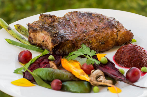用蔬菜、甜菜根和浆果酱在骨头上煎烤猪肉牛排。 在树叶的背景下