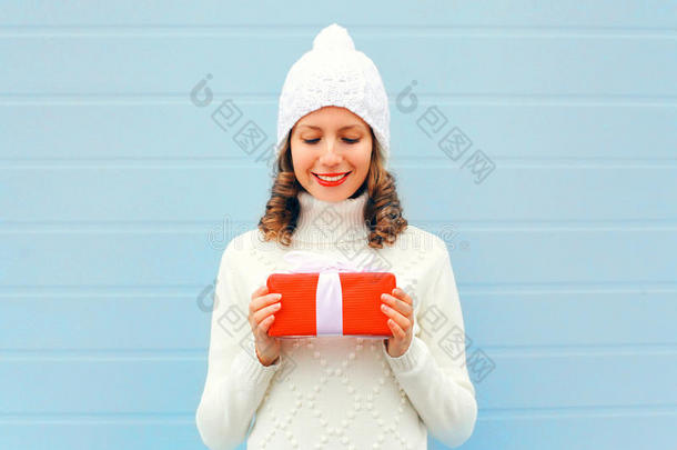 圣诞快乐微笑的年轻女子手拿礼品盒，身穿蓝色针织帽子毛衣