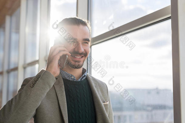 商务人员在手机上交谈，站在合作中心全景窗口前的商人