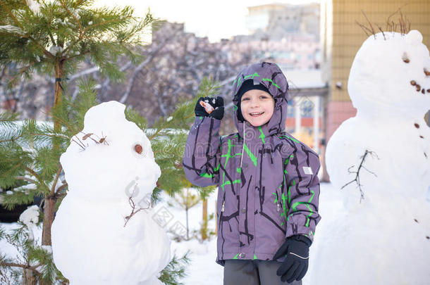 有趣的小男孩堆雪人，吃胡萝卜，玩雪，在寒冷的一天户外玩。 积极的休闲
