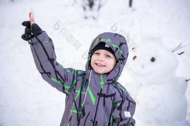有趣的小男孩堆雪人，吃胡萝卜，玩雪，在寒冷的一天户外玩。 积极的休闲