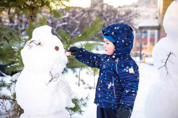 有趣的小<strong>男孩堆雪人</strong>，吃胡萝卜，玩雪，在寒冷的一天户外玩。 积极的休闲