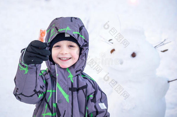 有趣的小男孩<strong>堆雪人</strong>，吃胡萝卜，玩雪，在寒冷的一天户外玩。 积极的休闲