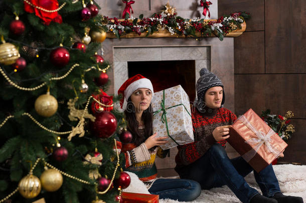 可爱的年轻一对猜测他们的圣诞礼物，拿着一个盒子在他的耳朵，当他们摇动它