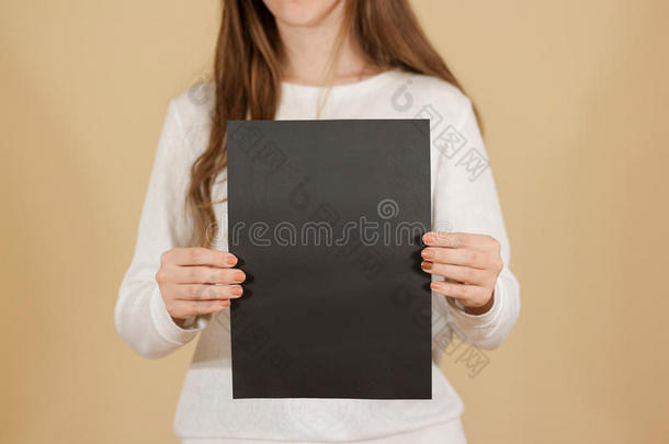 女孩垂直拿着黑色A4空白纸。 小册子介绍。 小册子牵着手。 女人显示清晰的偏移纸。 床单