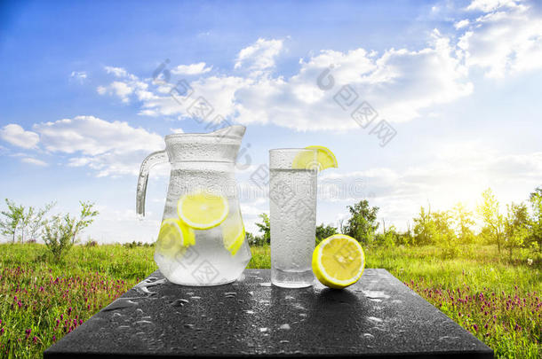 新鲜的冷水，柠檬和冰，放在桌子上的水罐里。把柠檬水和新鲜的柠檬水放在大自然的背景上。