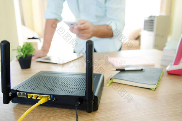 一个<strong>无线路由器</strong>的特写和一个在办公室客厅使用智能手机的男人