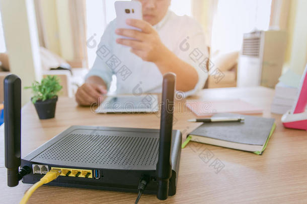 一个<strong>无线路由器</strong>的特写和一个在办公室客厅使用智能手机的男人