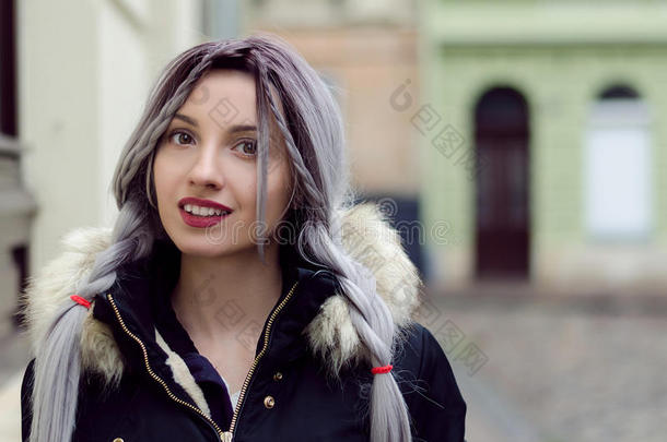 美丽的年轻女孩，银灰色的辫子，红色的嘴唇穿着黑色羽绒服，在温暖的冬天走在街上
