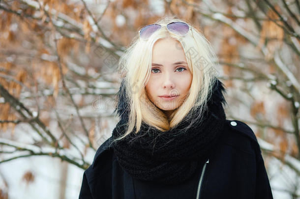 特写<strong>冬季</strong>肖像：年轻的金发女人穿着一件温<strong>暖</strong>的羊毛夹克，在雪城公园里摆着姿势，背上有树叶