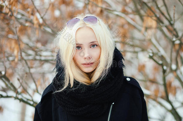 特写冬季肖像：年轻的金发女人穿着一件温暖的羊毛夹克，在雪城公园里摆着姿势，背上有树叶