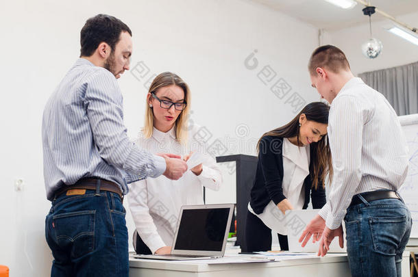 四个年轻的商业人士<strong>作为</strong>一个团队聚集在笔记本电脑周围，在一个开放的计划现代办公室