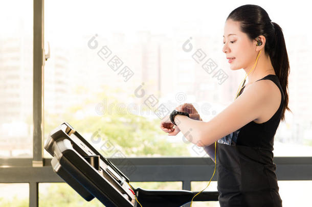 美丽的亚洲女人跑步跑步机使用智能手表听力