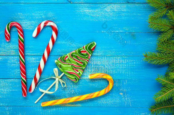 圣诞大餐：彩色棒棒糖，以<strong>云杉</strong>、糖果罐和绿色<strong>云杉</strong>树枝的形式出现在蓝色的木板上。