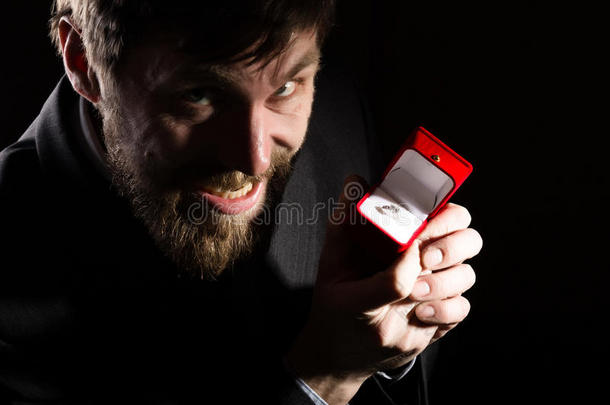 穿着西装的胡子男人在红色的盒子里给了一个戒指，并在黑暗的背景下表达了不同的情感