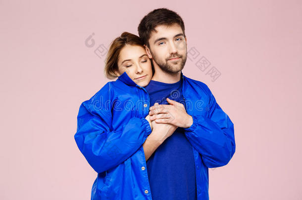 有趣的年轻漂亮夫妇穿着一件夹克，拥抱着浅<strong>粉色</strong>的背景<strong>微</strong>笑。