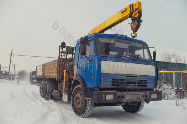 在晴朗的日子里，在白雪覆盖的冬季村庄用黄色起重机建造卡车