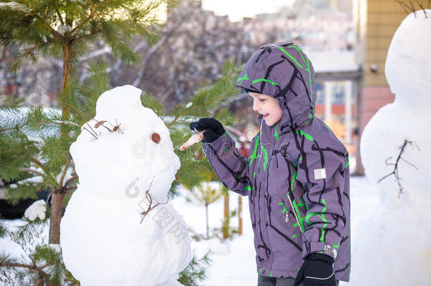 有趣的小男孩堆雪人，吃胡萝卜，玩雪，在寒冷的一天户外玩。 积极的休闲儿童