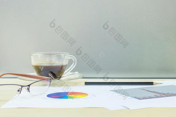 特写<strong>黑色</strong>咖啡在透明的咖啡杯与工作纸，铅笔和眼镜在模糊的木制桌子和<strong>磨砂</strong>玻璃