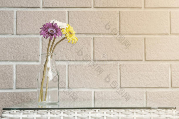 特写人工五颜六色的花在透明玻璃瓶上，在木桌上模糊的棕色砖墙纹理背景上