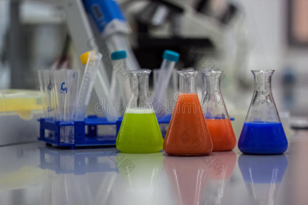 用于研究的生物技术实验室设备。 烧瓶，瓶子和吸管与彩色橙色，绿色和蓝色液体和