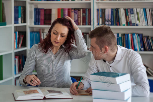 美丽的红头发女孩和英俊的金发男孩在图书馆办公室的一个项目上工作，与打开的书讨论项目和