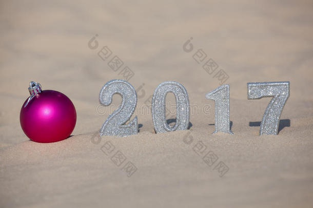 四个新年`的身影在沙滩或海边的沙滩上，在地上投下了一个巨大的阴影。 沙子附近是粉红色的球。