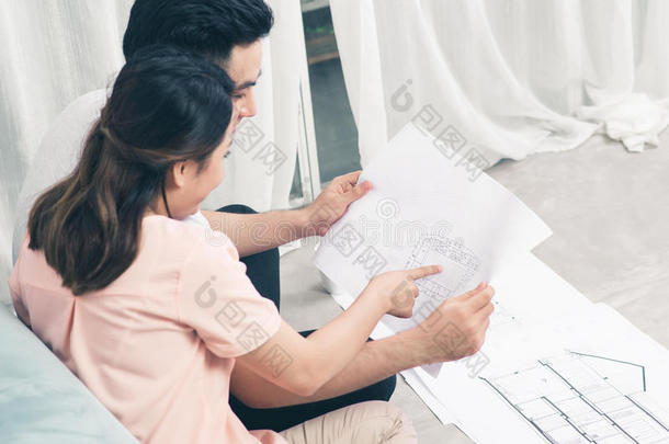 一对年轻漂亮的亚洲成年夫妇正在<strong>看房</strong>子的设计图。