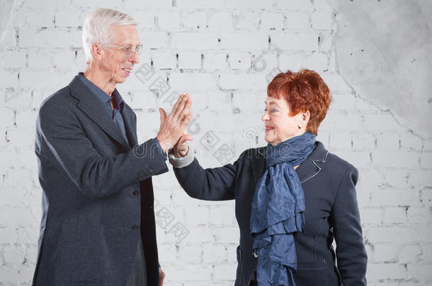 给一个击掌。 幸福微笑的老夫妇站在一起拥抱在一起，孤立在白色的砖块背景上。 复制空间。