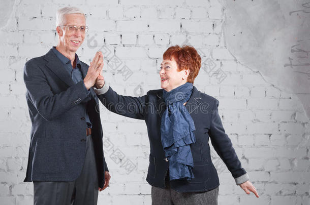 给一个击掌。 幸福微笑的老夫妇站在一起拥抱在一起，孤立在白色的砖块背景上。 复制空间。