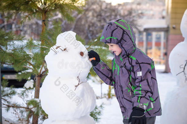 有趣的小<strong>男孩堆雪人</strong>，吃胡萝卜，玩雪，在寒冷的一天户外玩。 积极的休闲儿童