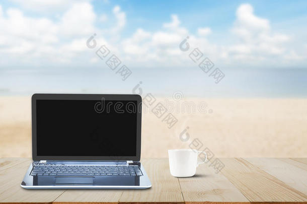 电脑笔记本电脑，黑色屏幕和热咖啡杯在木制<strong>桌面上</strong>模糊的海滩背景