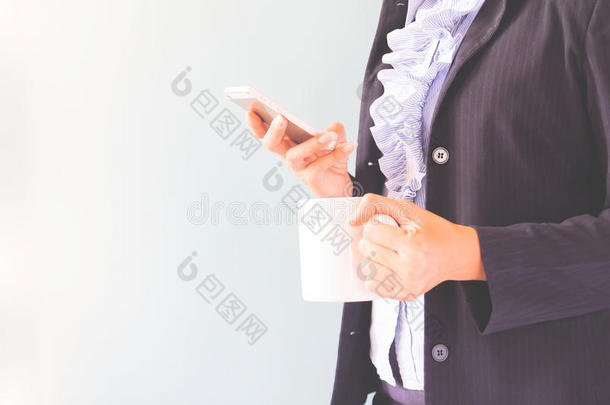商务女士穿着深色西装，拿着手机和咖啡，商业理念