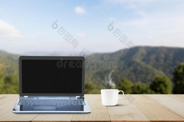 电脑笔记本电脑与黑色屏幕和热咖啡杯在木制桌面上模糊的山背景