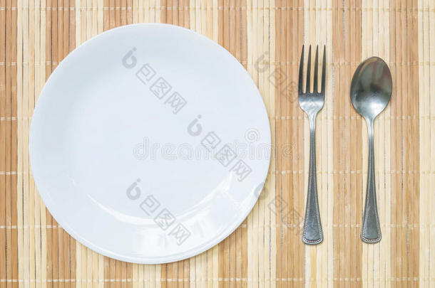 特写白色陶瓷菜肴与不锈钢叉子和勺子在木<strong>垫</strong>纹理<strong>背景</strong>在餐<strong>桌</strong>上的顶部视图