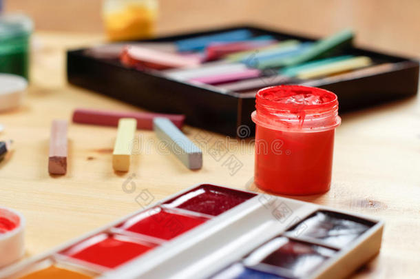 一罐打开的水粉，水彩，蜡笔躺在一张木桌上。