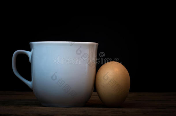 鸡蛋和一个杯子放在木地板上。 背景黑蛋，
