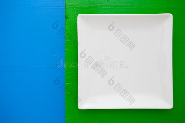 蓝色和绿色背景上的空白色陶瓷盘子，方形盘子