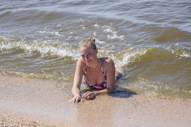 金发女孩穿着<strong>比基尼</strong>躺在海滩上，海浪溅在上面。 美丽的年轻女人穿着五颜六色的<strong>比基尼</strong>在海上背景