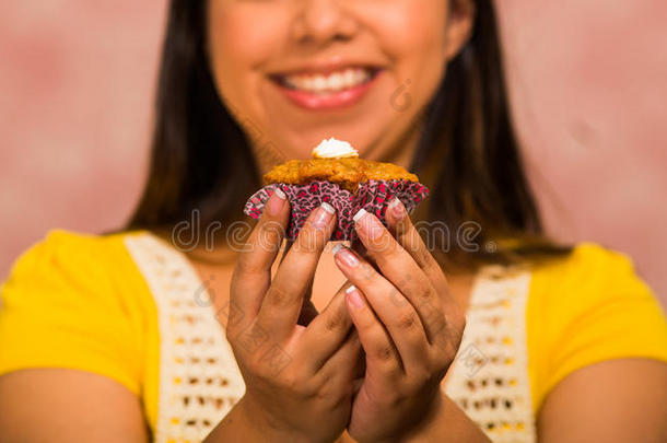 黑发女人拿着美味的棕色松饼，上面有奶油，<strong>大大</strong>的微笑，准备咬一口，糕点