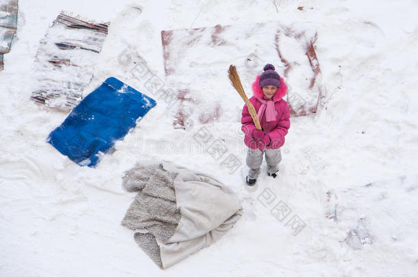 可爱的小女孩用扫帚在雪地上清理垫子和地毯