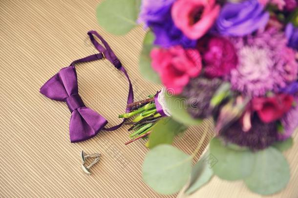 美丽的婚礼紫色花束与<strong>胸针</strong>和新郎保龄球袖扣在米色椅子上