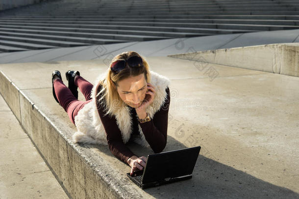 美丽的年轻女人特写。 金发女孩坐在办公室外的台阶上，拿着一块平板电脑。 带笔记本的女人。